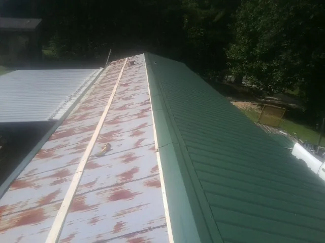 Old rusted panels beside newly installed green metal roofing — Wind Damage Roof Repair by Roofing Brothers in Silt