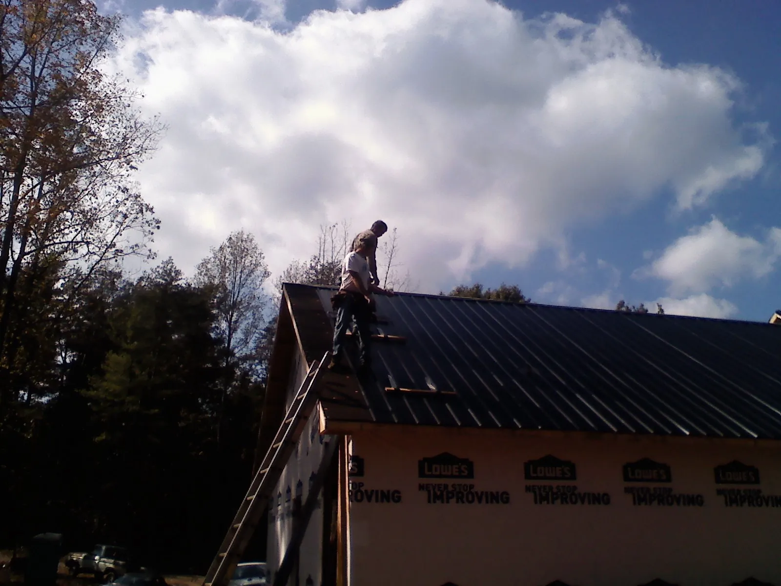 Roofer fastening dark metal panels high against a cloudy sky, from a Roof Inspection job in Silt