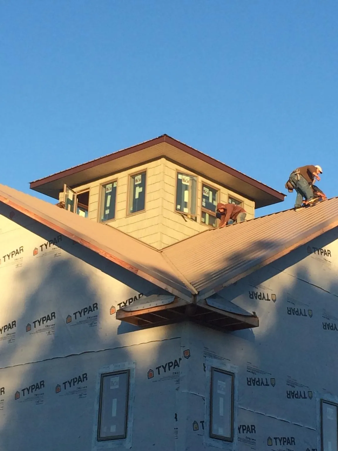 Roofers working around a rooftop cupola on a new metal roof at sunset in Silt